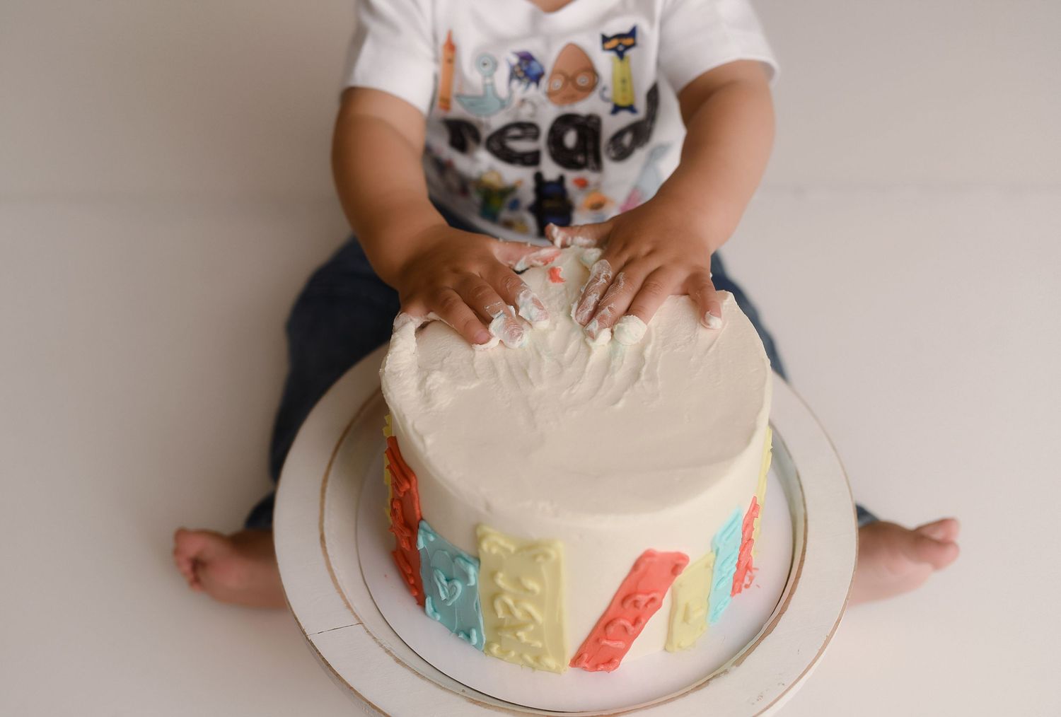 Baby smashing a white frosted birthday cake with colorful decorations during a first birthday cake smash photoshoot.