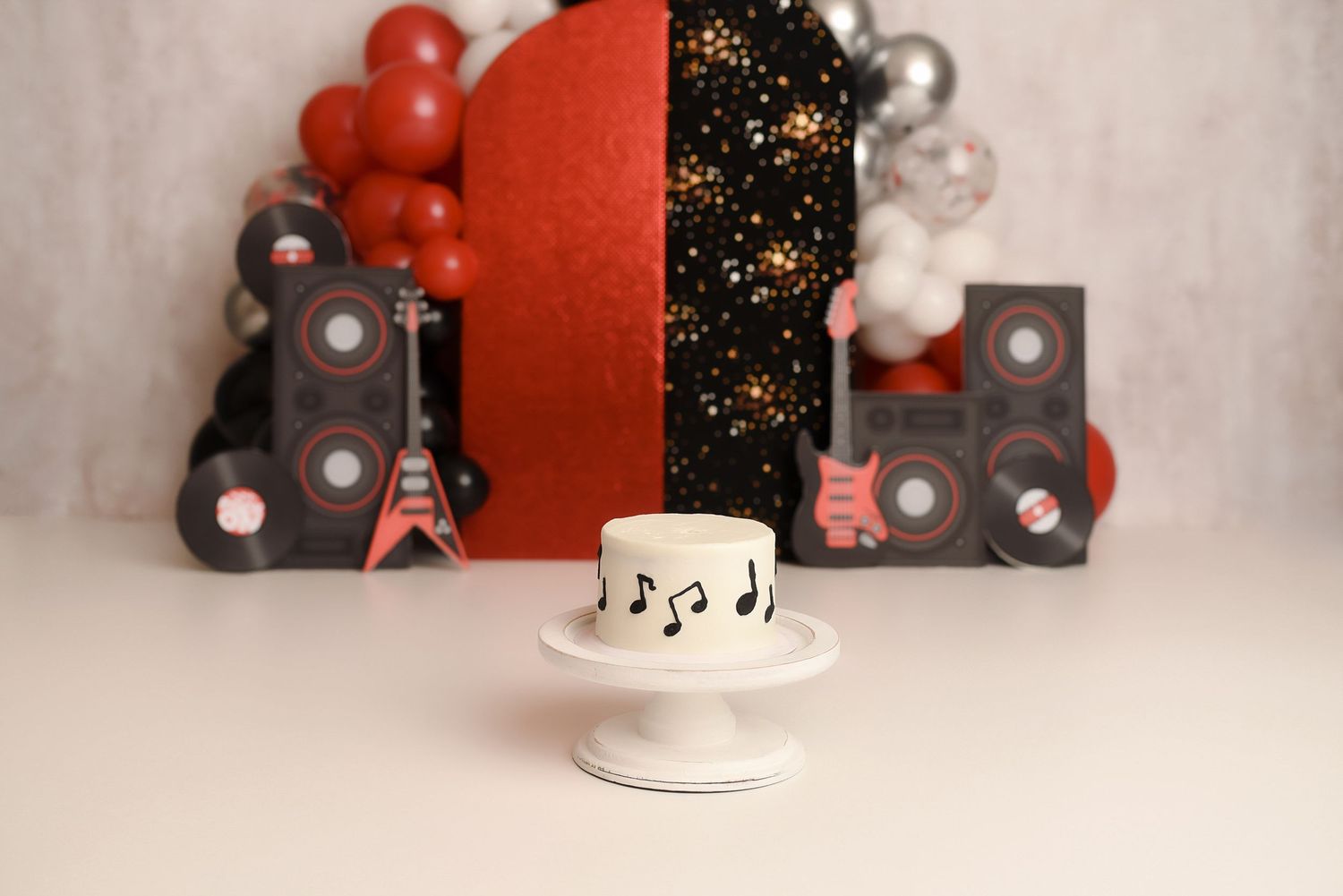 Rock and roll themed first birthday cake with musical notes on white stand with guitar and speaker decor.