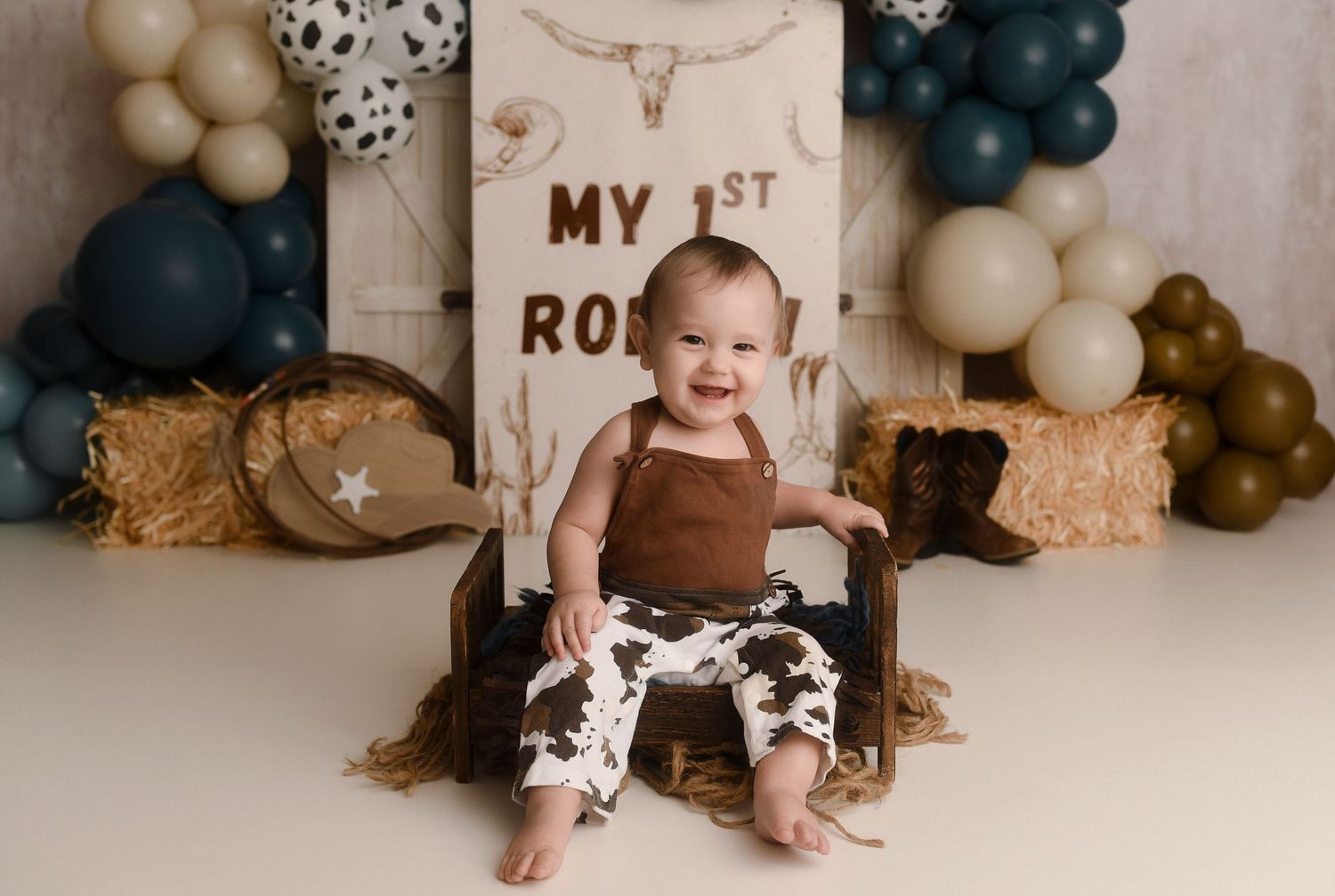 Baby boy sits in wooden crate at western cowboy first birthday rodeo cake smash photo session.