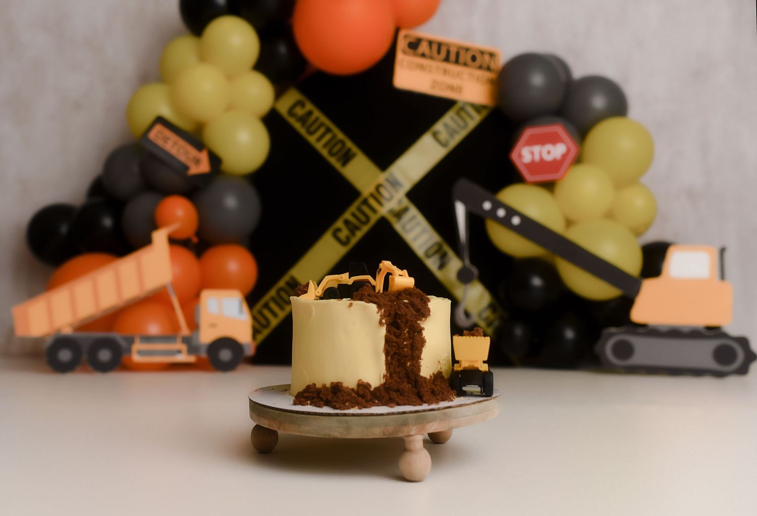 Construction themed smash cake with yellow frosting and chocolate crumbles, surrounded by dump truck decorations and caution tape balloons.