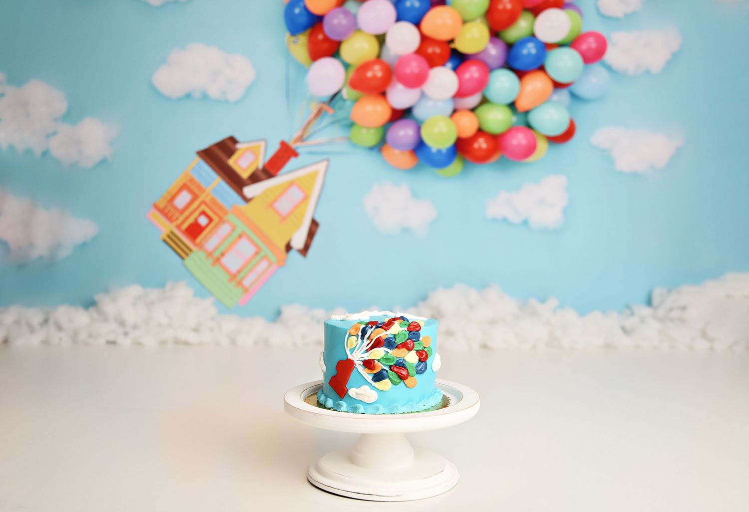 Disney Pixar Up-themed first birthday smash cake with floating house topper and colorful balloon backdrop.