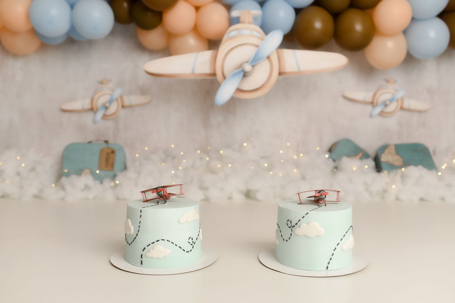 Two matching light blue first birthday cakes with airplane decorations displayed at a twins cake smash setup.