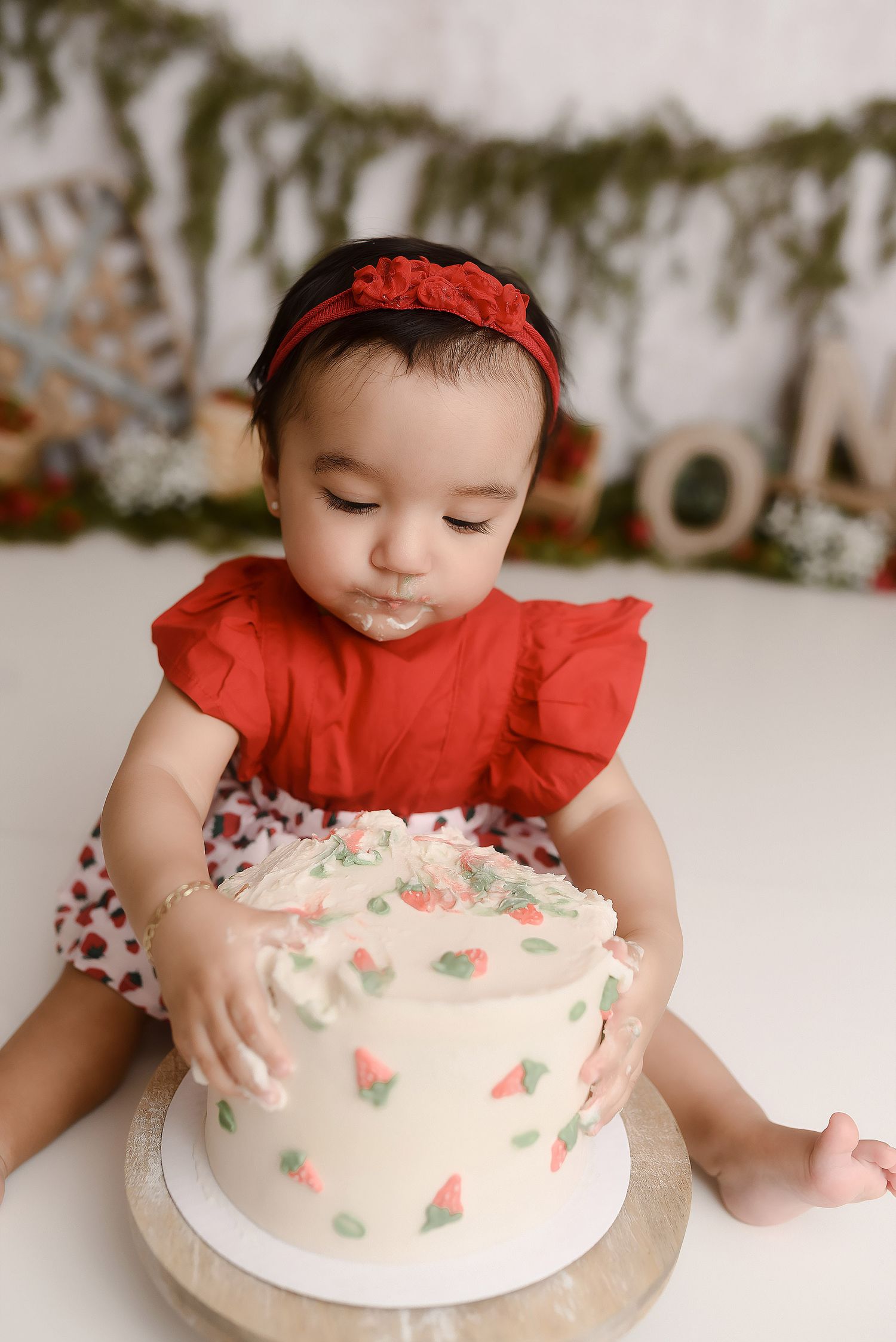 One year old girl in red dress touching strawberry decorated cake at first birthday cake smash.