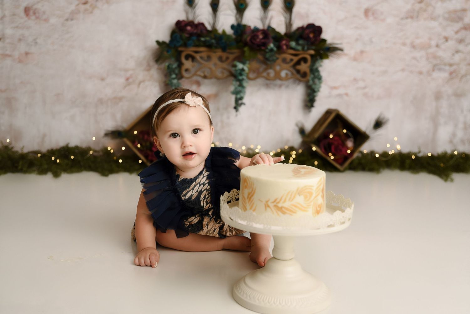 Baby girl in navy dress with white smash cake and Christmas holiday garland backdrop.