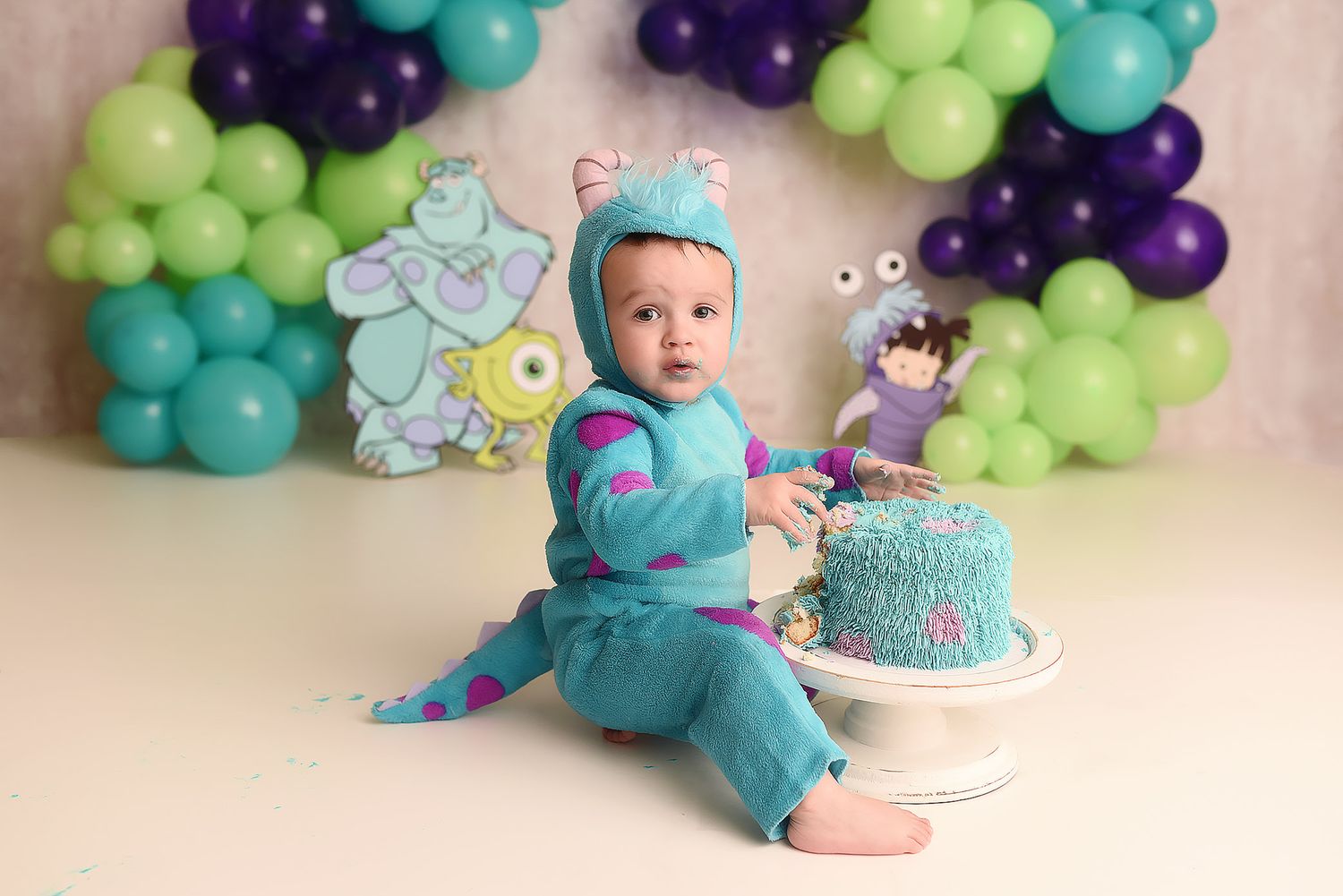 Baby boy in Sulley Monsters Inc costume with matching smash cake and balloon backdrop.