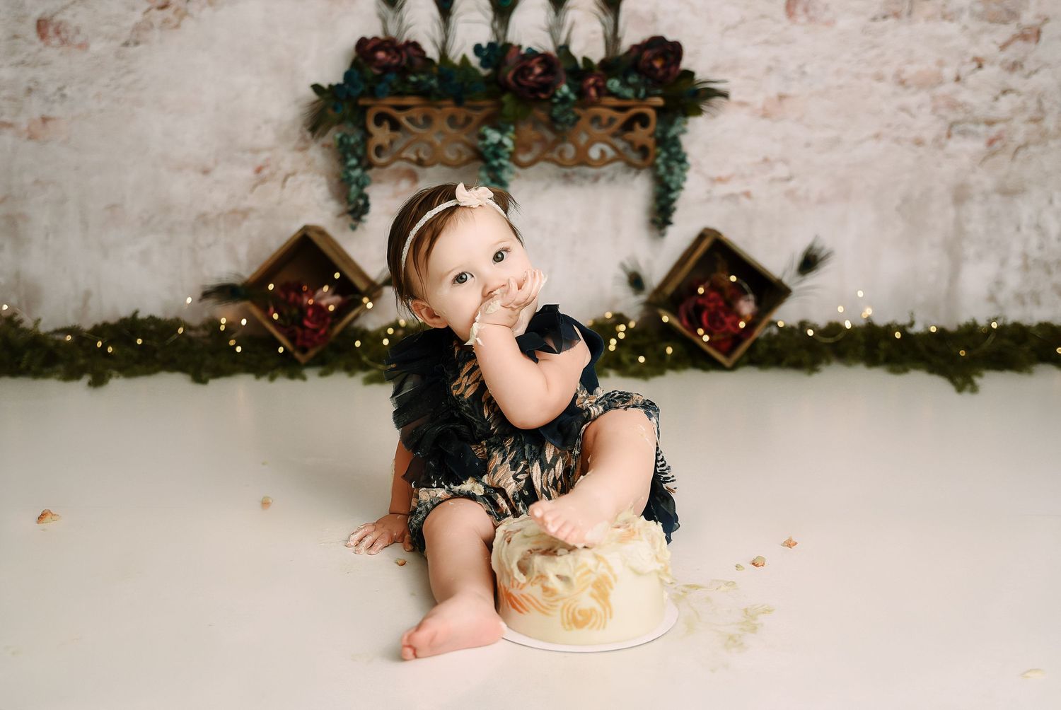 Baby girl eating smash cake in navy dress with festive Christmas holiday backdrop.
