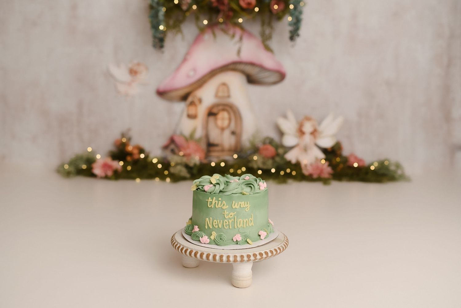 Green fairy tale mushroom first birthday cake with floral and fairy decorations on white cake stand.