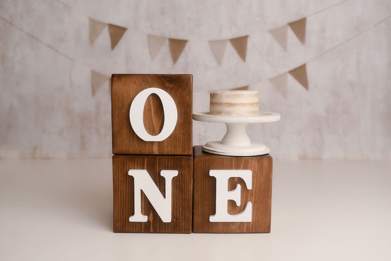 Wooden ONE blocks with white letters beside a cake stand, perfect for a first birthday photo shoot.