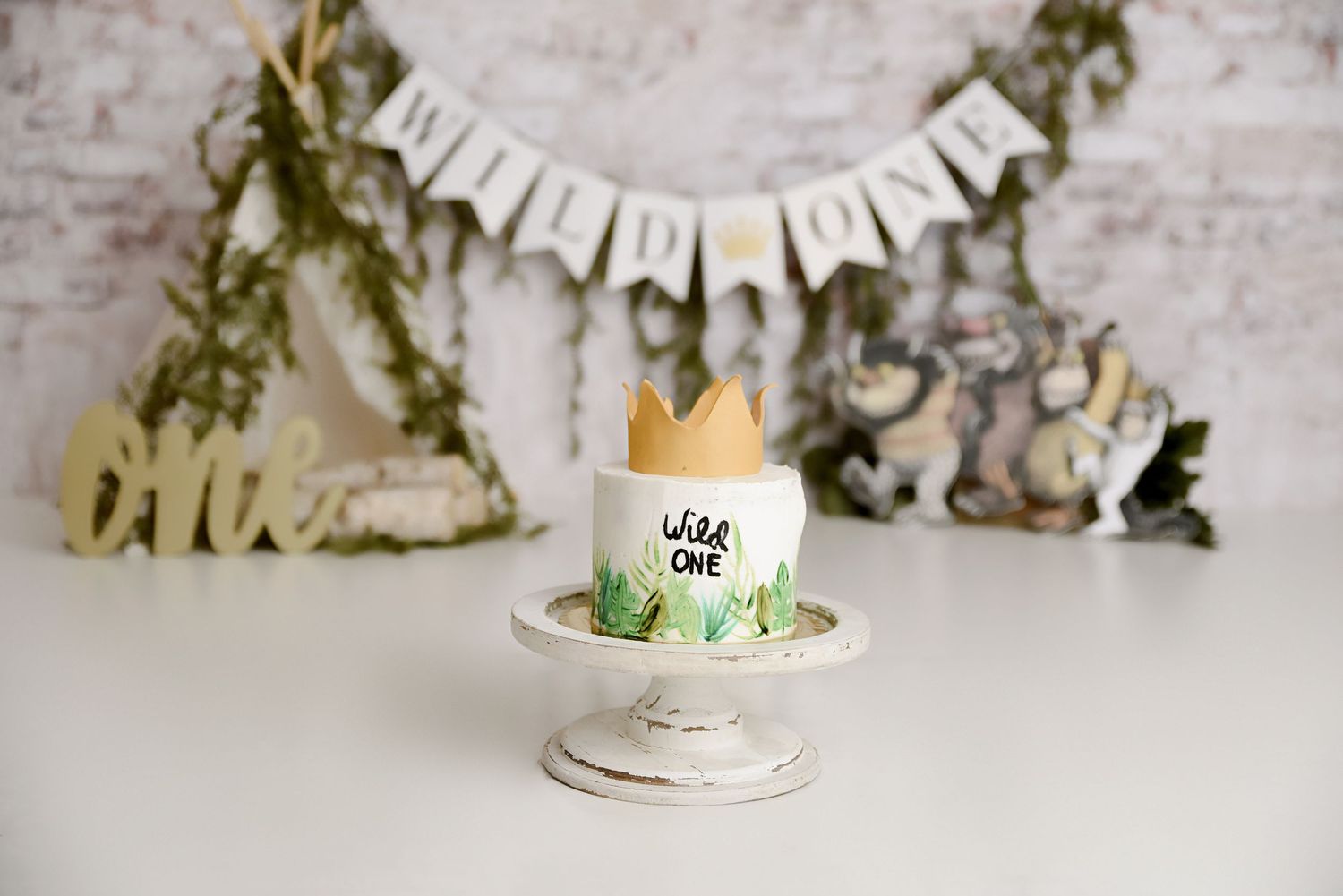 Wild One first birthday smash cake with crown on white stand and teepee backdrop.