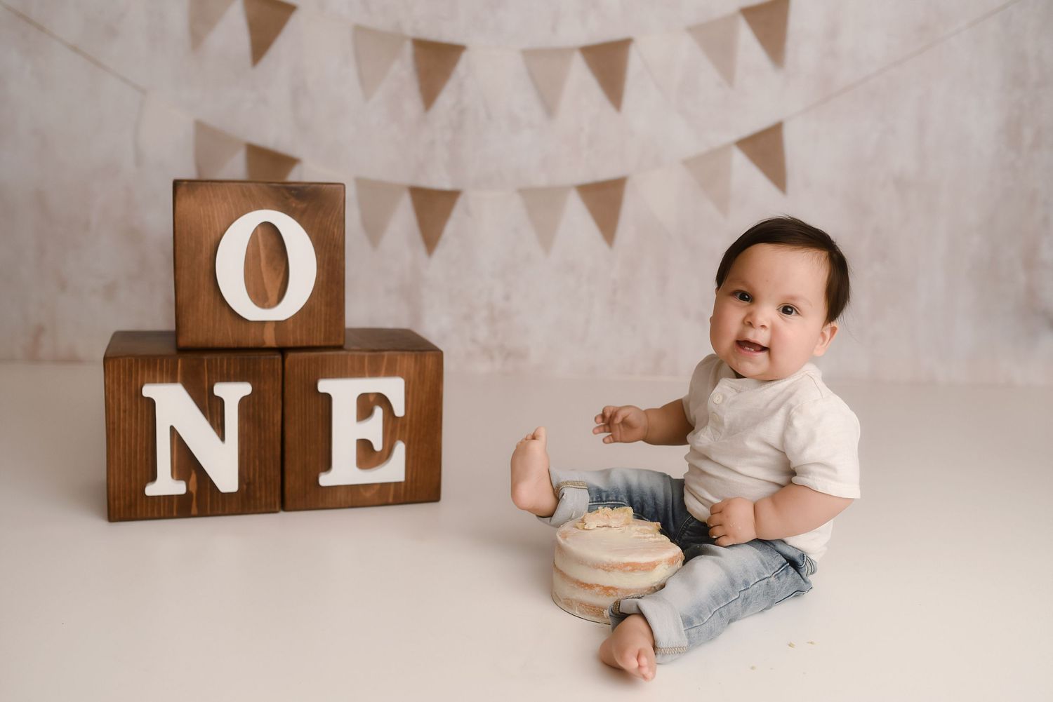 Baby's first birthday cake smash photo with wooden ONE blocks and bunting banner backdrop.