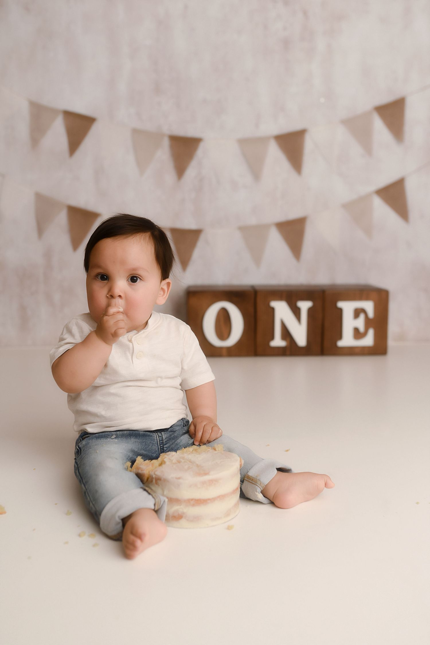 Baby boy celebrates first birthday smashing cake, sitting in front of ONE blocks and bunting decorations.