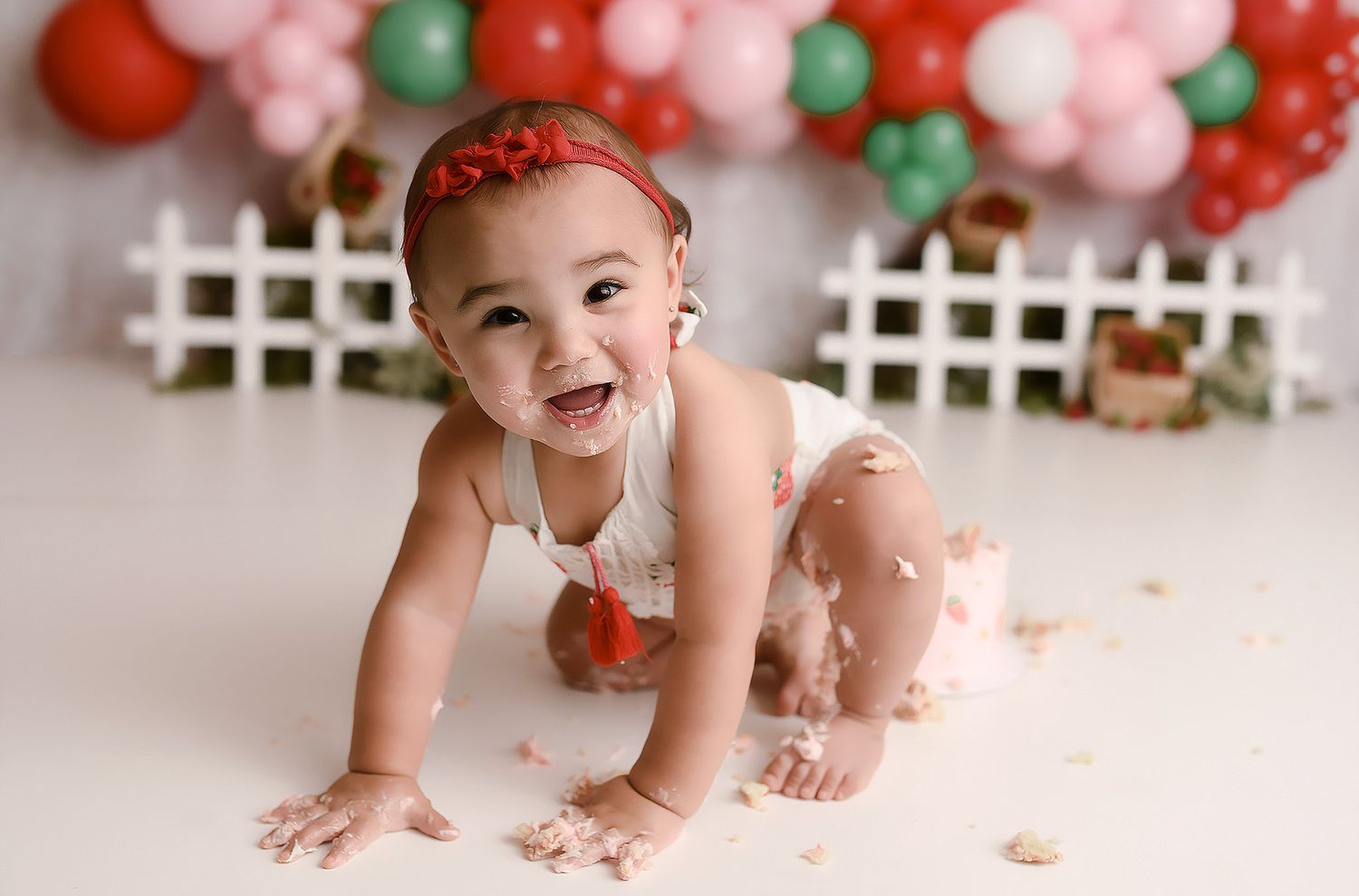 Happy baby girl crawling and smiling during strawberry themed cake smash photoshoot.