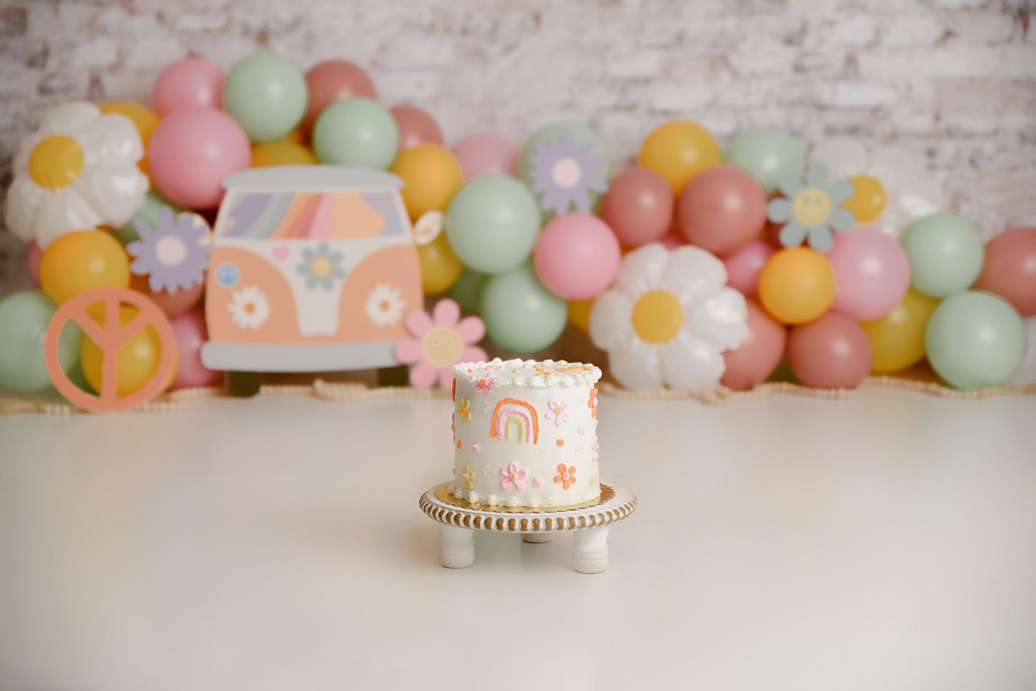 Colorful groovy retro rainbow smash cake with VW bus and daisy balloon backdrop.