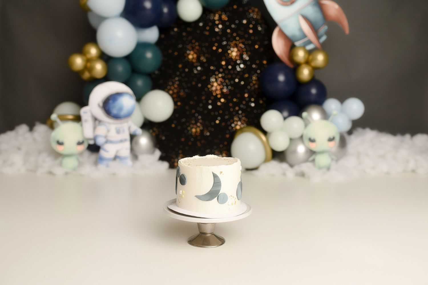 White first birthday cake with moon and star designs at a space-themed cake smash with astronaut decorations.