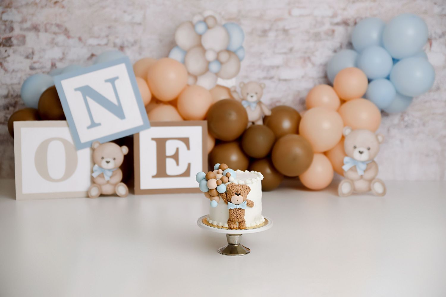 Teddy bear first birthday smash cake with ONE blocks and balloon garland backdrop.