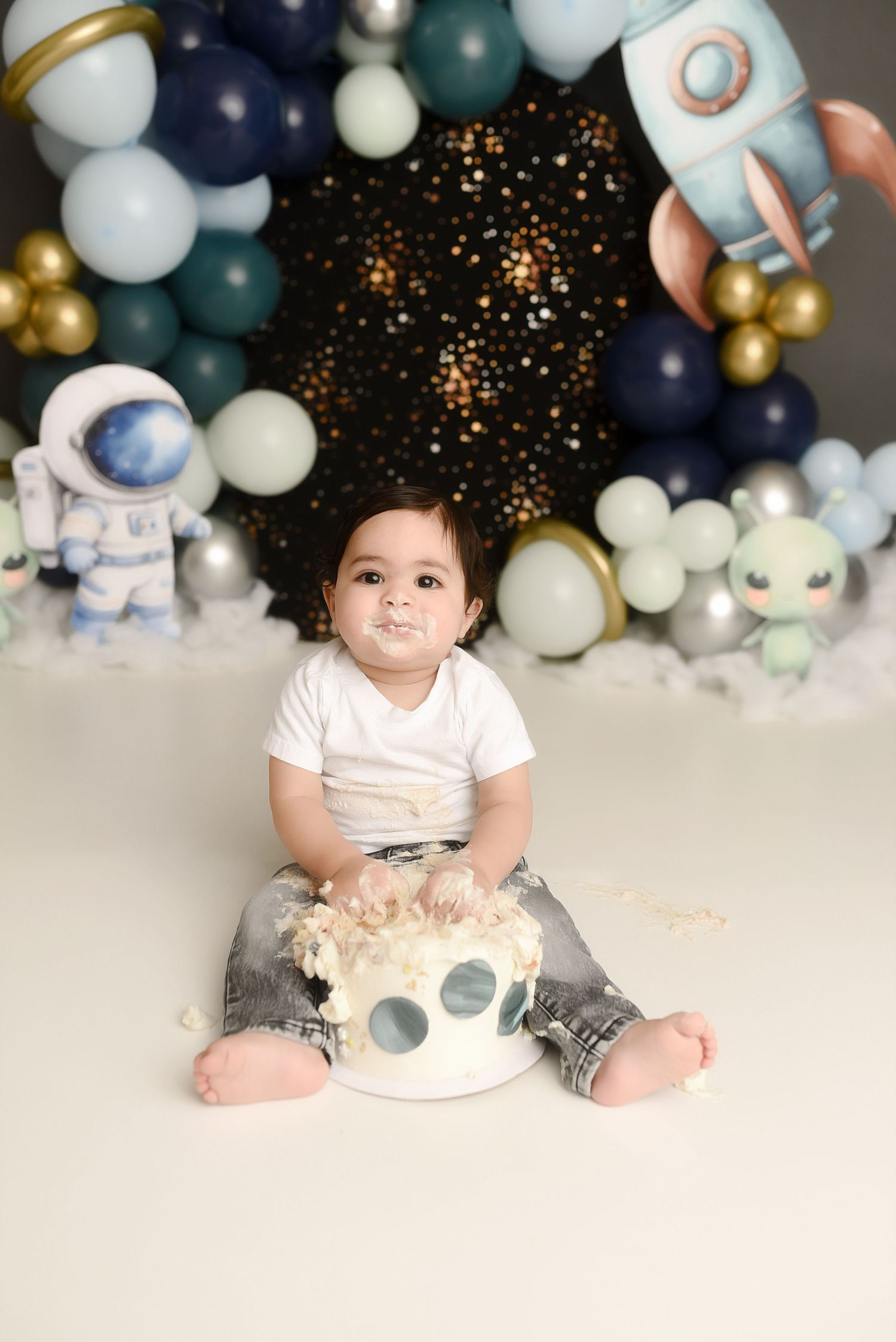 Baby's first birthday cake smash with space theme, balloons, rocket, and astronaut decorations in blue and gold.