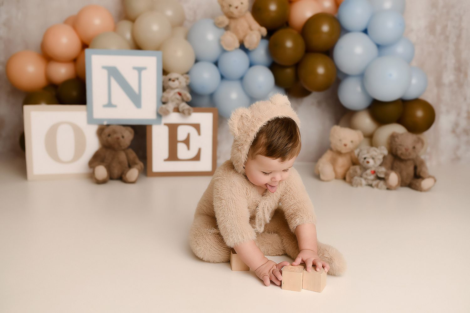 Baby boy in bear outfit playing with blocks at a teddy bear themed first birthday cake smash photo session.