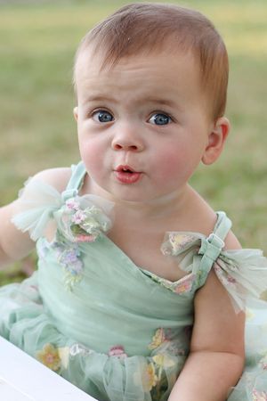 Baby in mint green dress makes silly faces while posing for a series of playful photos outdoors.