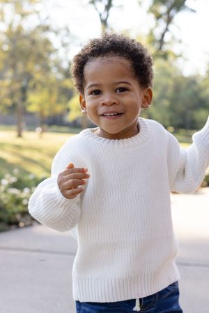 A collage of four photos showing a child in a white sweater and jeans smiling and playing outdoors on a sunny day.