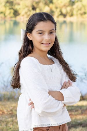 A person in a white lace-trimmed top poses outdoors near a lake during golden hour.