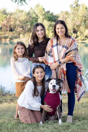 Family portrait session at sunset by a lake with their white and brown pitbull dog wearing a burgundy sweater.
