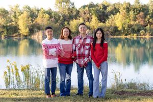 A group in matching blue jeans and red tops poses together by a serene lake during golden hour.