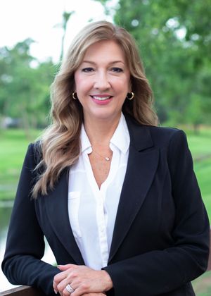 Professional business portrait outdoors with black blazer and white blouse against green natural background.