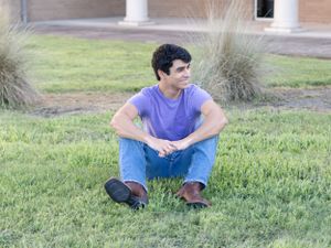 Someone wearing a purple t-shirt sits cross-legged on grass with ornamental grasses in the background.