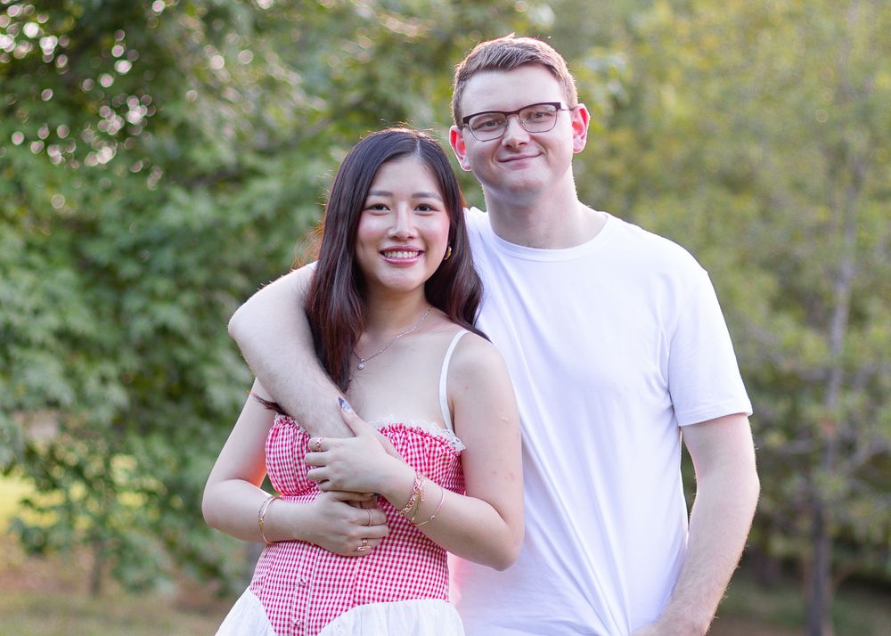 A couple embraces outdoors while wearing matching red and white outfits against a blurred natural background.