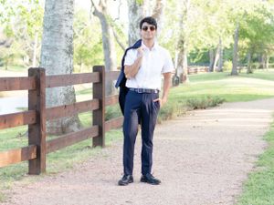 A person in a white shirt and dark pants stands on a gravel path next to a wooden fence in a park setting.