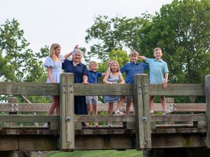 A family group poses together on a wooden bridge against a backdrop of green summer trees.