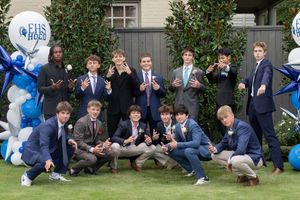 A group of people in formal attire sit and relax together on grass outside a building.