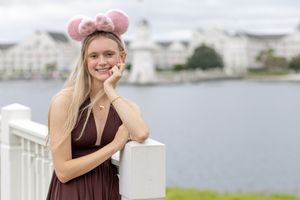 A person in a burgundy dress poses on a white railing near a waterfront on a cloudy day.