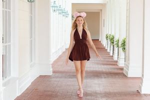 A person in a burgundy outfit walks down a bright white columned hallway with arched windows.
