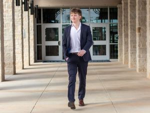 Student in navy blazer and white shirt walks confidently through modern building columns.