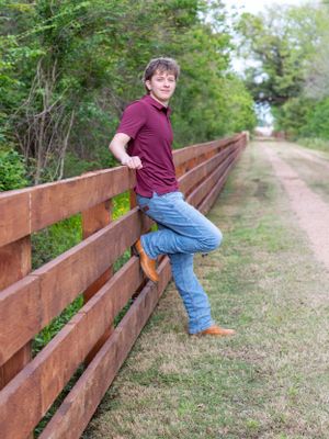 Casual portrait of someone leaning against a wooden fence on a nature trail.