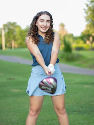 Person in a blue top and tennis skirt poses playfully on a grassy field.