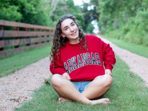Person in an Arkansas sweatshirt sits cross-legged on a path with wooden railings.