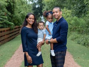 Family of four poses together on outdoor trail with wooden fence.
