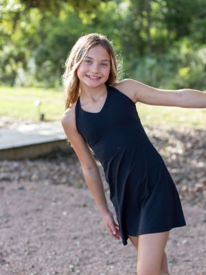 Person in black dress poses playfully outdoors.