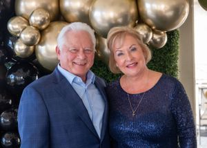 Couple poses together in formal attire against gold balloon backdrop.