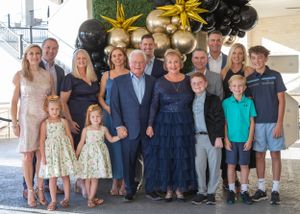A large family group poses together for a formal photo against a backdrop with gold and black balloons.