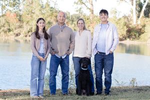 Family group poses together outdoors in casual attire by a scenic lake during golden hour.