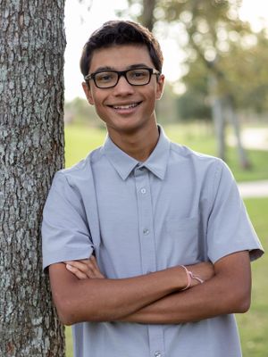 Portrait of a young person in a light blue shirt leaning against a tree trunk.