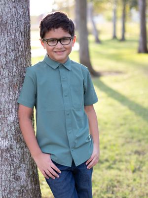 Portrait of a young person in a teal shirt posing against a tree in a park setting.