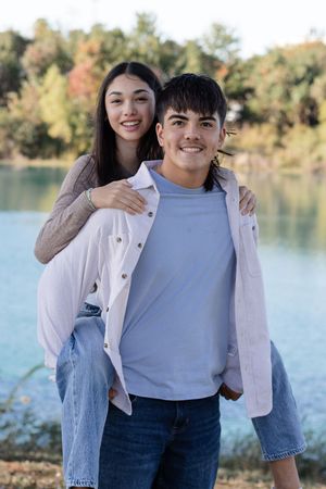 A couple shares a tender moment by a scenic lake on an autumn day, wearing casual denim and light colored tops.