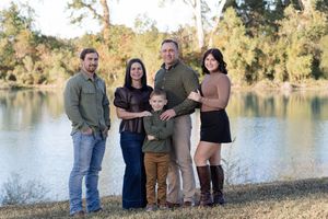 A family poses together on the shore of a serene lake during golden hour with trees in the background.