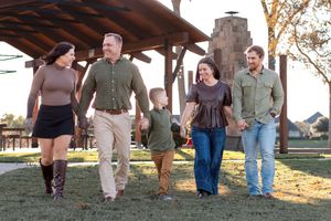 A group walks together outdoors at sunset under a wooden pavilion on a grassy lawn.