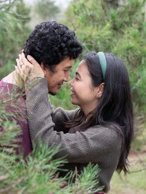 A romantic couple shares an intimate moment among pine trees.