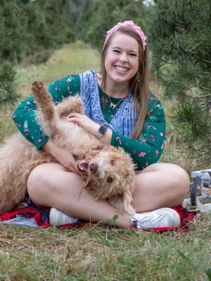 A person plays with a happy golden doodle dog lying on its back on a red blanket.